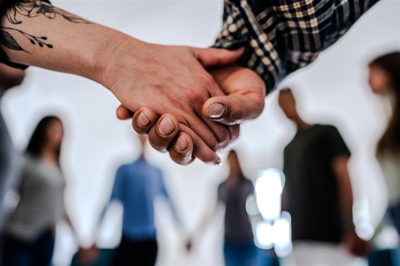Close-up of people holding hands supporting each other during a group session.