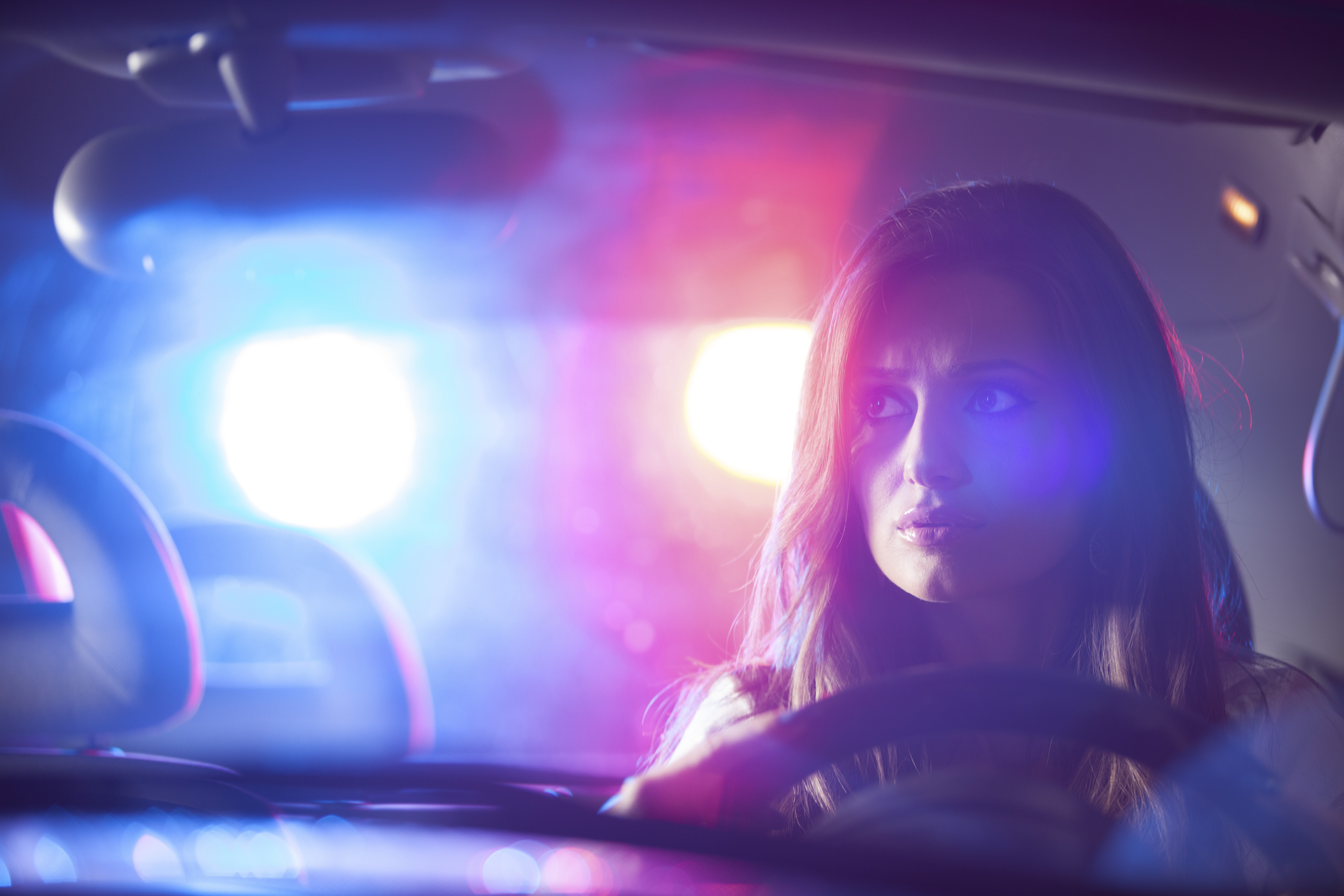 A driver inside a car with police lights flashing behind the vehicle.