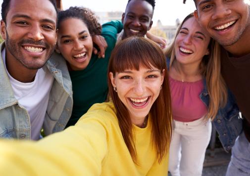 Group of diverse youth taking a selfie outdoors, having fun in sunny day.