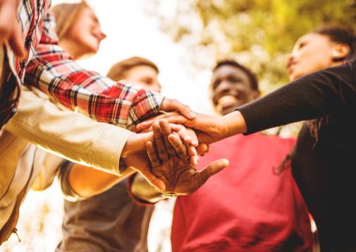 Group of people standing in a circle with their hands stacked together in a team gesture.