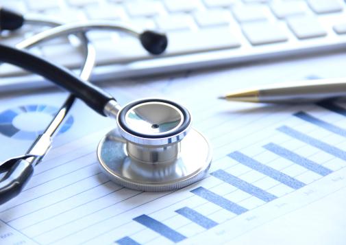 Stéthoscope et stylo posés sur des dossiers médicaux, à côté du clavier d’un ordinateur. 
