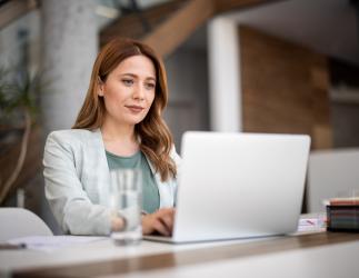 woman in white blazer watching a computer screen. 