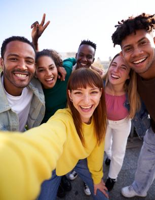 Group of diverse youth taking a selfie outdoors, having fun in sunny day.