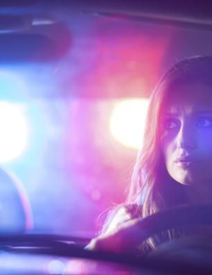 A driver inside a car with police lights flashing behind the vehicle.