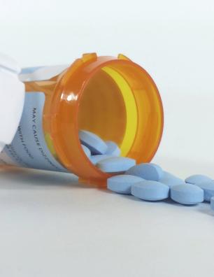 Orange prescription bottle tipped over with blue oval pills spilling onto a white surface.