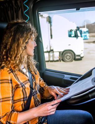 Femme portant une chemise jaune à carreaux assise dans la cabine d’un camion qui lit des documents sur un porte-bloc reposant sur le volant.