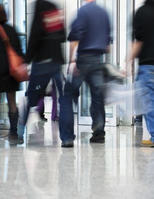 Blurred motion of people walking through a modern glass entrance in a busy urban building lobby.