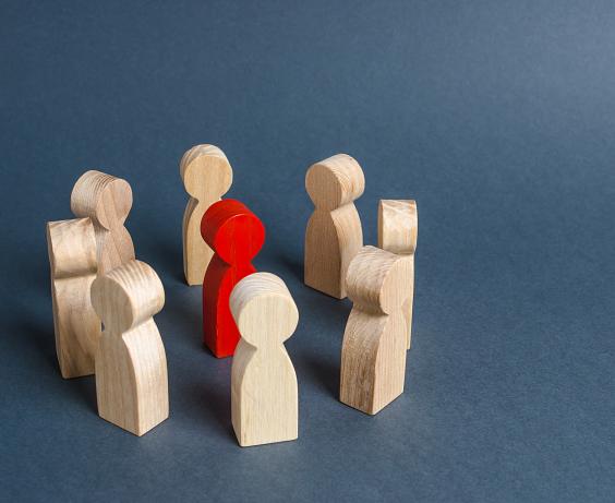 Wooden figurines in a circle surrounding a single red figurine.
