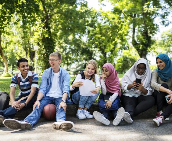 Youth sitting outside on a sidewalk.