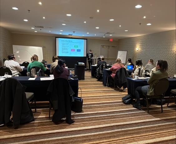 Salle de conférence avec les participants à l'atelier assis à des tables face à un présentateur au premier rang.