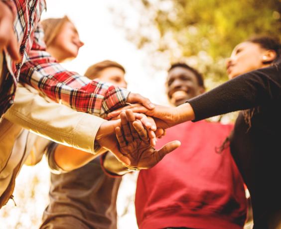 Group of people standing in a circle with their hands stacked together in a team gesture.