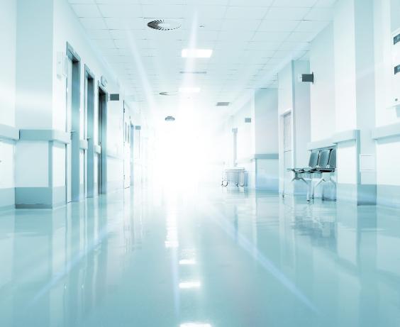 Bright, empty hospital hallway with reflective floors and doors lining both sides.
