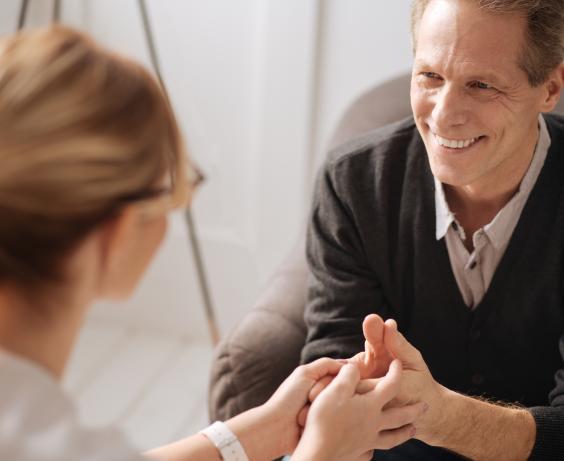 Two people sitting close together, with one person holding the other’s hands in a supportive conversation. 