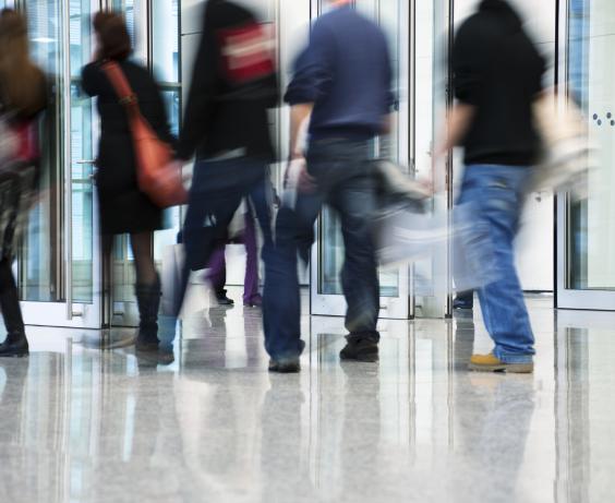 Blurred motion of people walking through a modern glass entrance in a busy urban building lobby.
